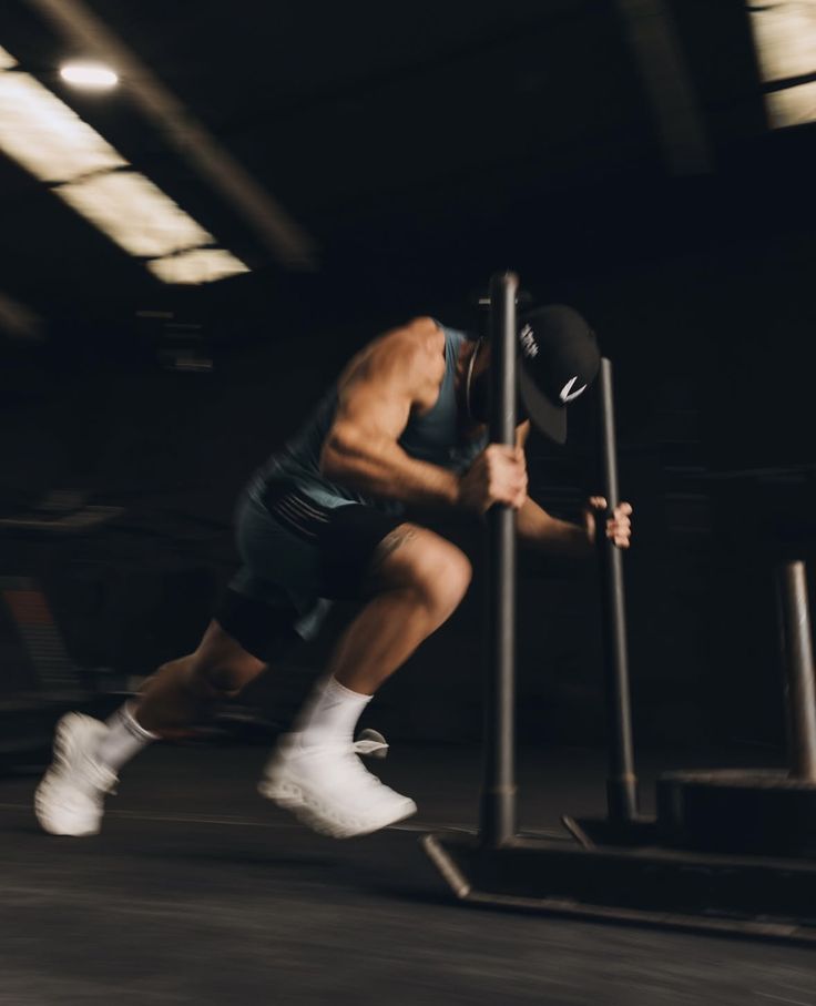 An athlete driving a weighted sled across a dark gym floor